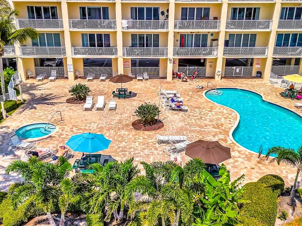 Aerial view of the inviting pool deck, featuring a sparkling main pool, hot tub, and tropical landscaping—a relaxing central courtyard perfect for sunbathing and unwinding during your stay.