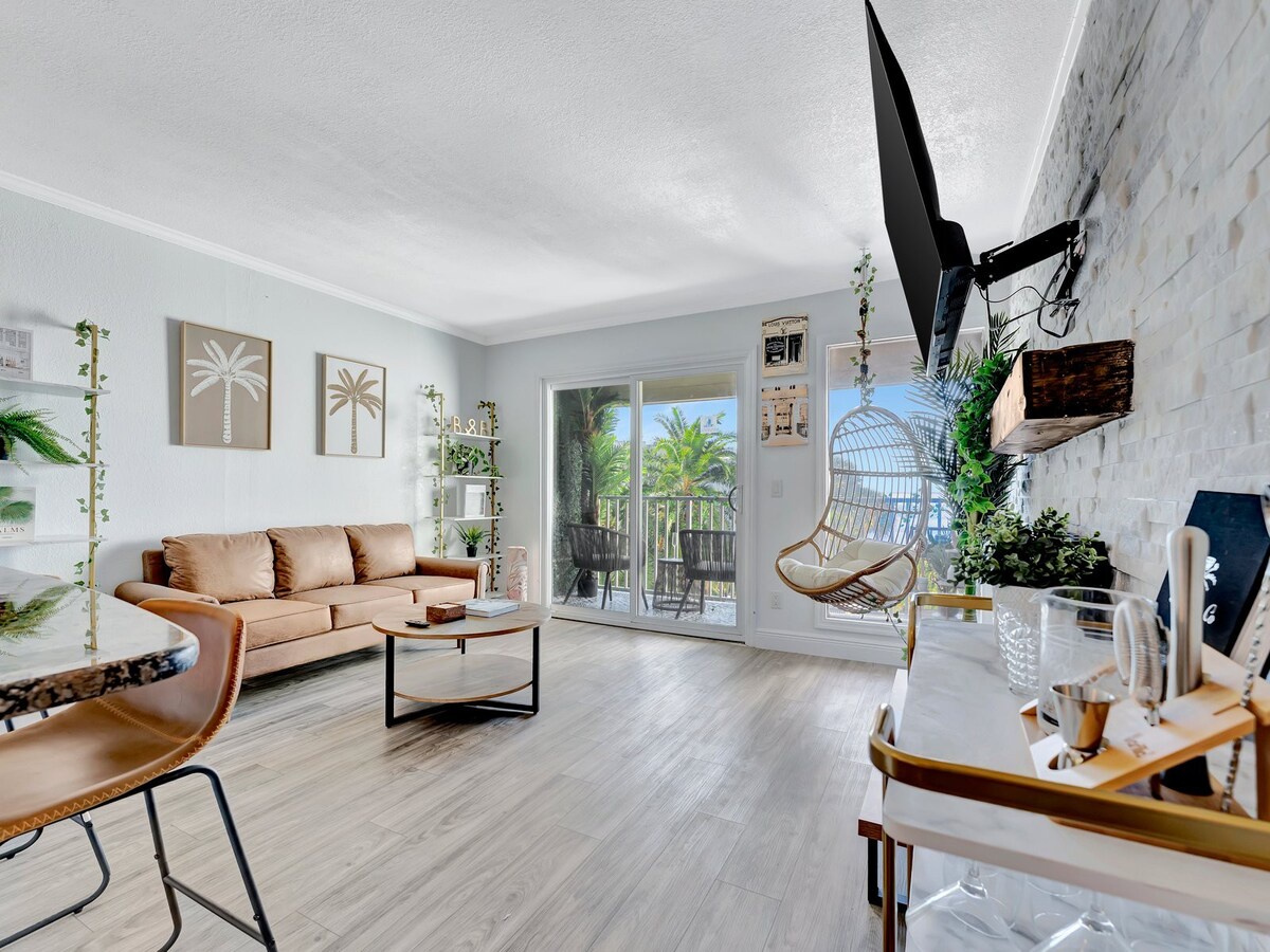 Step into your tropical sanctuary, where palm-inspired décor and lush greenery create a serene retreat. Relax on the plush sofa or swing gently in the hanging chair as natural light fills the space and reveals your private balcony oasis.