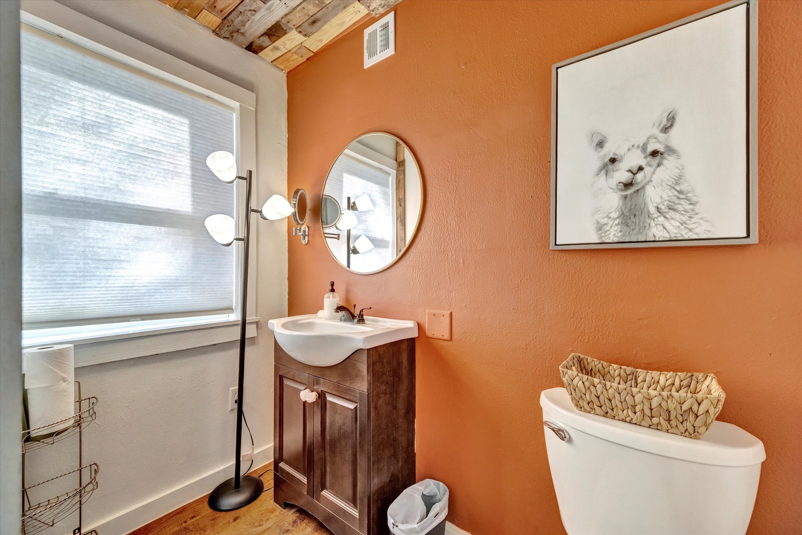 Freshen up in your charming bathroom with warm terracotta walls, rustic wood vanity, and natural light from the frosted window. The whimsical llama art and exposed beam ceiling add character to this cozy space.