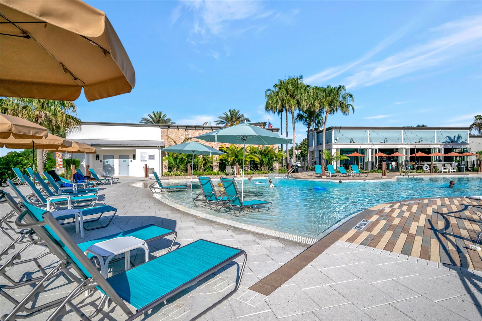Relax poolside under swaying palms, where your lounge chair awaits beneath a shaded umbrella. The inviting water sparkles under blue skies, surrounded by tropical landscaping and nearby dining.