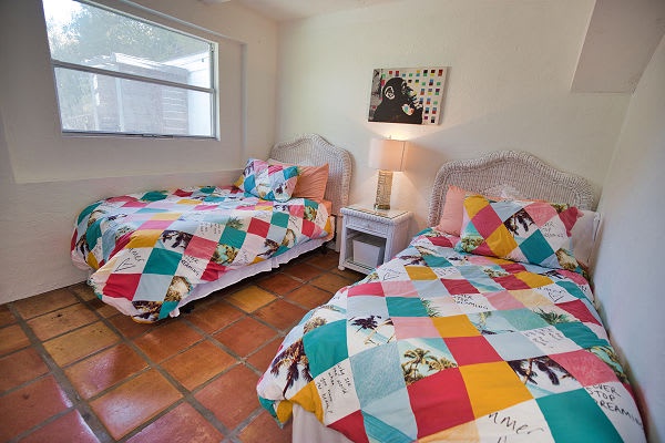Your perfect retreat for the kids awaits—bright, cheerful twin beds dressed in playful quilts, natural light streaming in, and a warm terracotta floor inviting rest and adventure.