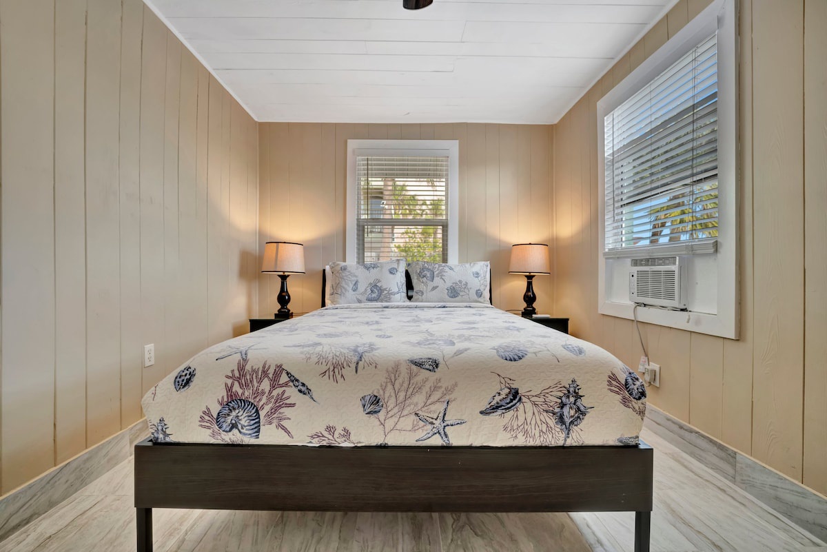 Step into your serene coastal retreat, where soft nautical linens and warm wood tones create the perfect sanctuary for restful nights. Natural light filters through the windows, inviting the peaceful rhythm of beach life into your private escape.