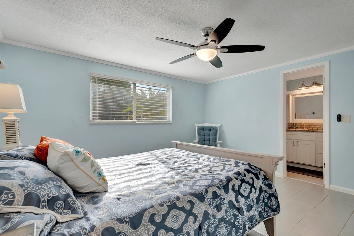 Your restful bedroom offers cool blue tones and breezy comfort. A ceiling fan keeps the air fresh while natural light streams in through bright windows.