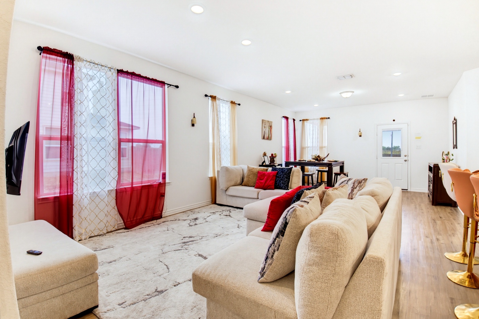 Spacious living area with plush sectional seating and natural light from colorful curtains. Open layout flows seamlessly into the dining space, perfect for gathering with loved ones.