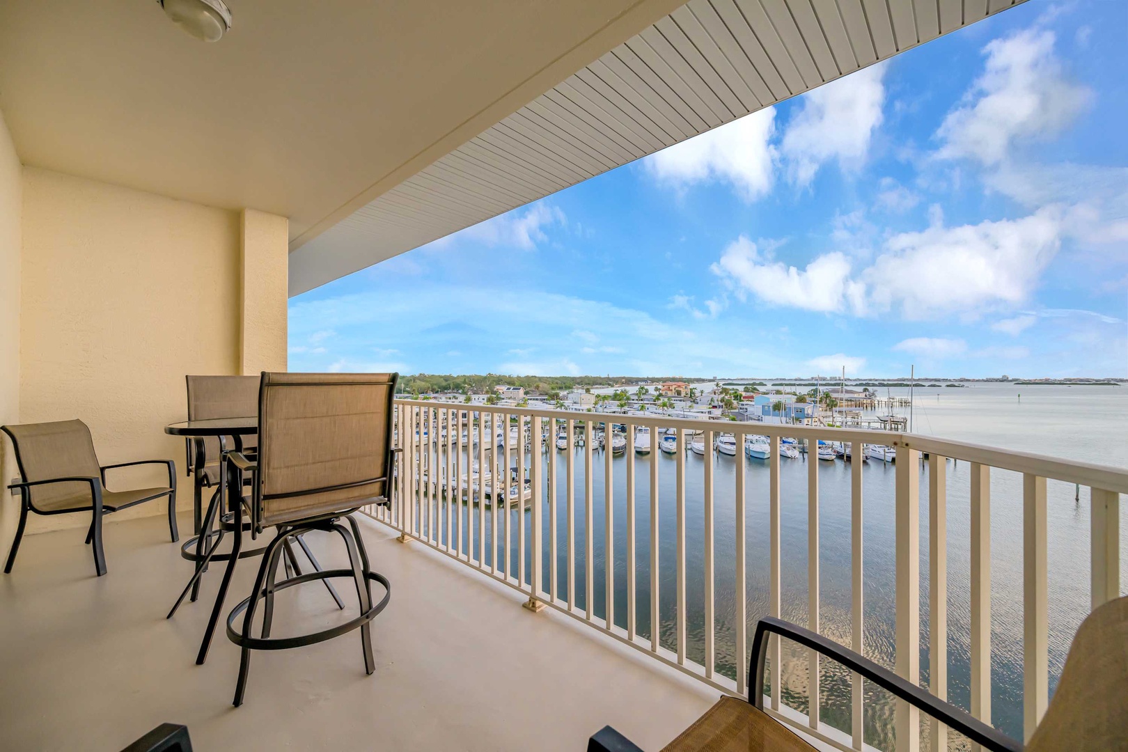 A covered balcony overlooks a peaceful marina with rows of docked boats and waterfront homes stretching along the horizon under open skies.