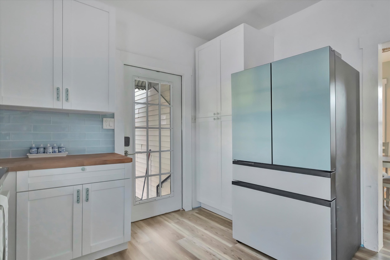 Your bright kitchen features clean white cabinetry, warm wood counters, and a sleek modern refrigerator. Light pours in through charming French doors that lead to your outdoor space.