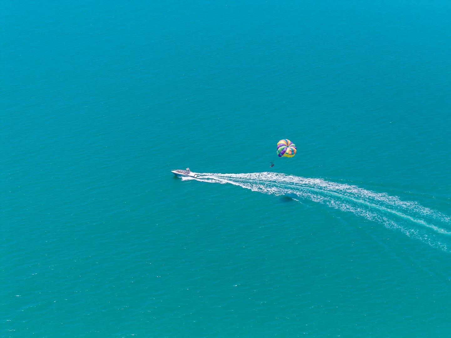 Aerial view of a speedboat towing a parasail over crystal-clear turquoise waters near the property.