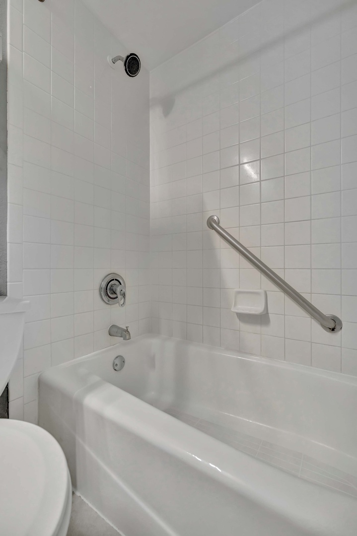 Step into your private bathroom featuring a tub-shower combo with accessibility grab bars for your comfort and safety. Crisp white tiles create a clean, refreshing space for your morning routine.