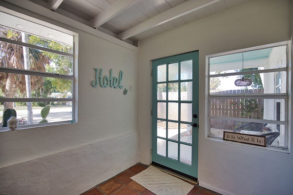 A bright, welcoming entry with palm trees just outside. Notice the charming vintage hotel sign and the cheerful teal door that leads you to your coastal getaway.