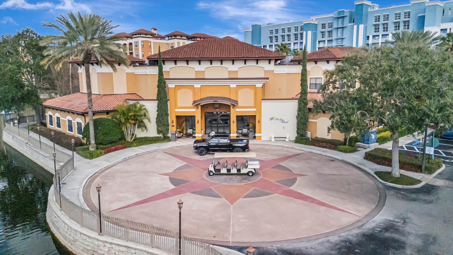 Arrival at the property begins with a grand entrance courtyard featuring Mediterranean-style architecture and a welcoming porte-cochère, surrounded by lush palm trees and manicured landscaping.