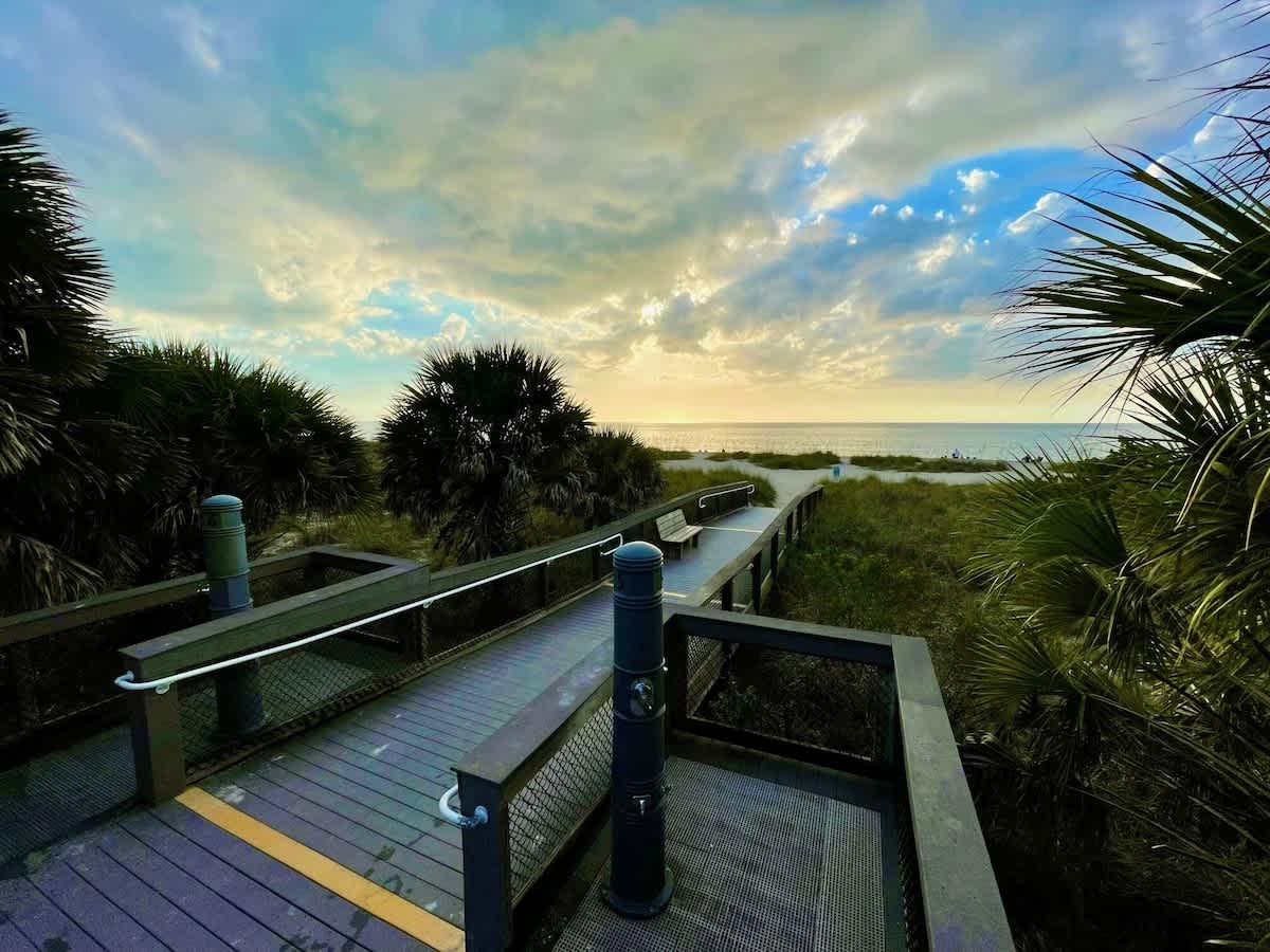 This accessible boardwalk path winds through coastal palms and dunes to a serene beachfront, offering a tranquil escape where golden sunsets meet the ocean horizon.