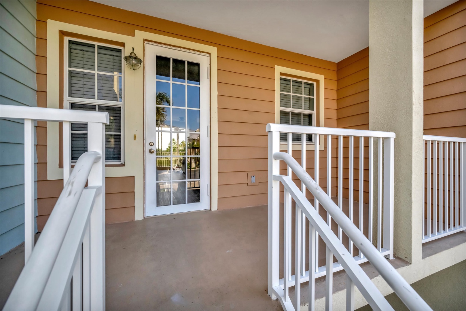 Step onto your private balcony with inviting outdoor space framed by crisp white railings. The glass door reflects swaying palms and sunshine, giving you a preview of the relaxed coastal vibe waiting just outside.