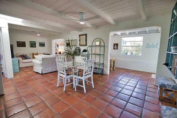 Step into your open-concept retreat, where soft terracotta tiles and beamed ceilings meet coastal charm. Gather around the dining table, unwind in the living area, or let natural light guide you to the cozy bedroom beyond.