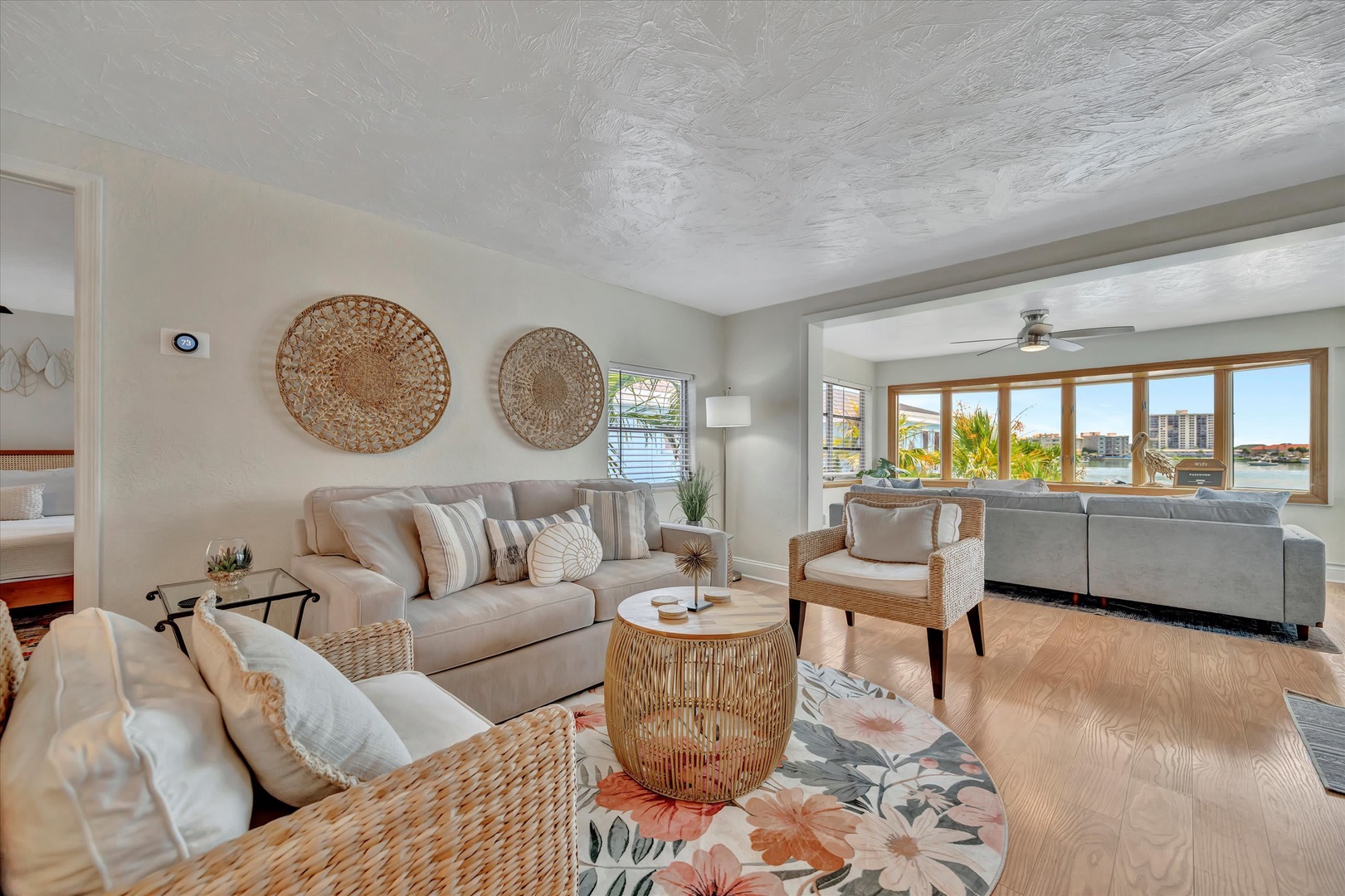 Relax in your bright, coastal-inspired living room where natural textures and soft neutrals create a calming retreat. Large windows frame waterfront views, filling the space with sunshine and inviting breezes.