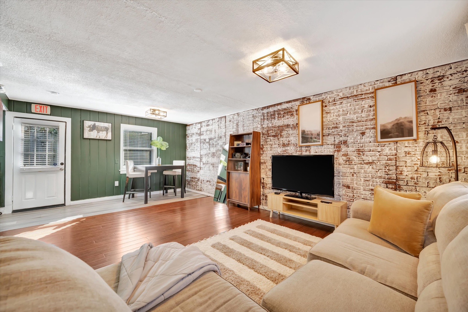 Sink into plush seating and unwind in your cozy living room, where warm wood floors meet rustic exposed brick. The space invites you to relax with friends or curl up for a quiet evening at home.