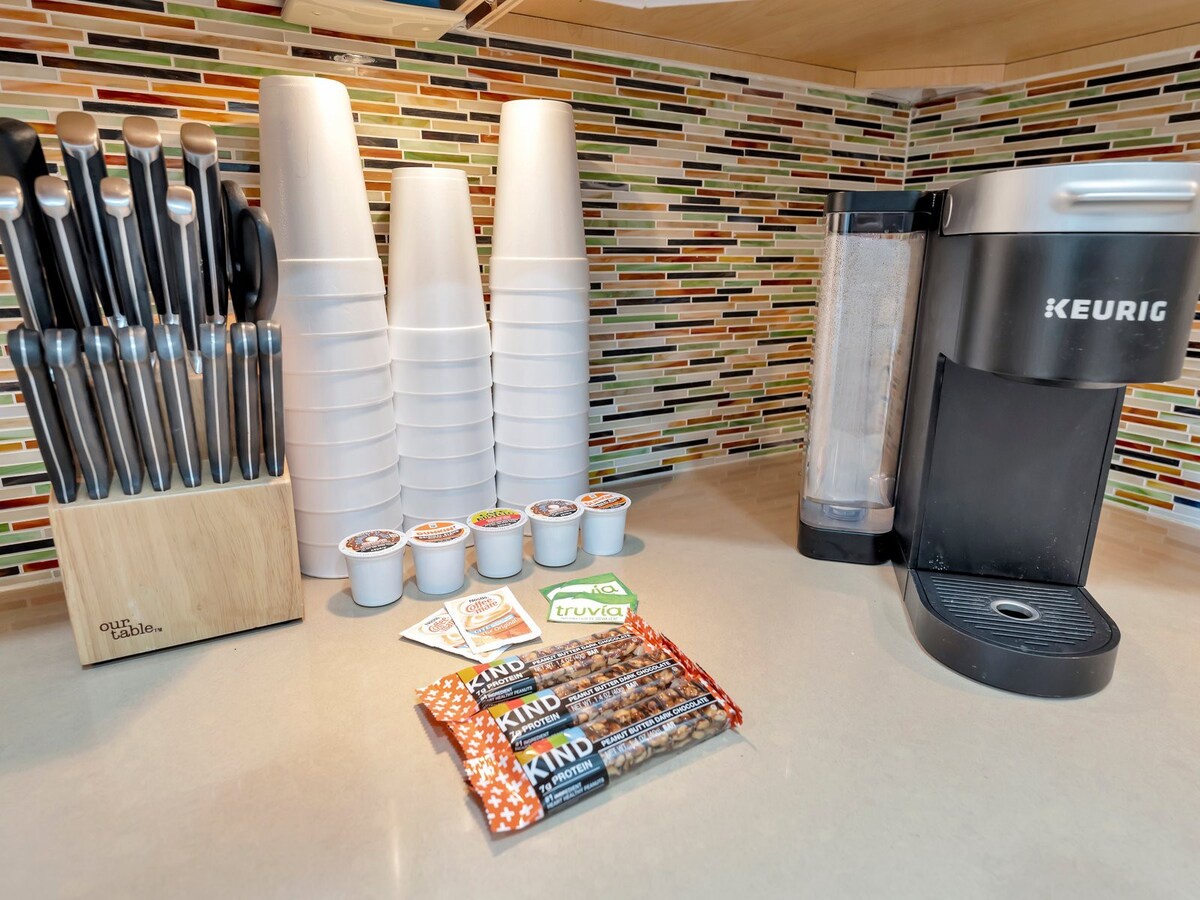 Your morning coffee is ready when you are—a sleek Keurig brewer, fresh pods, and plenty of cups await on the counter, with snack bars to fuel your day.