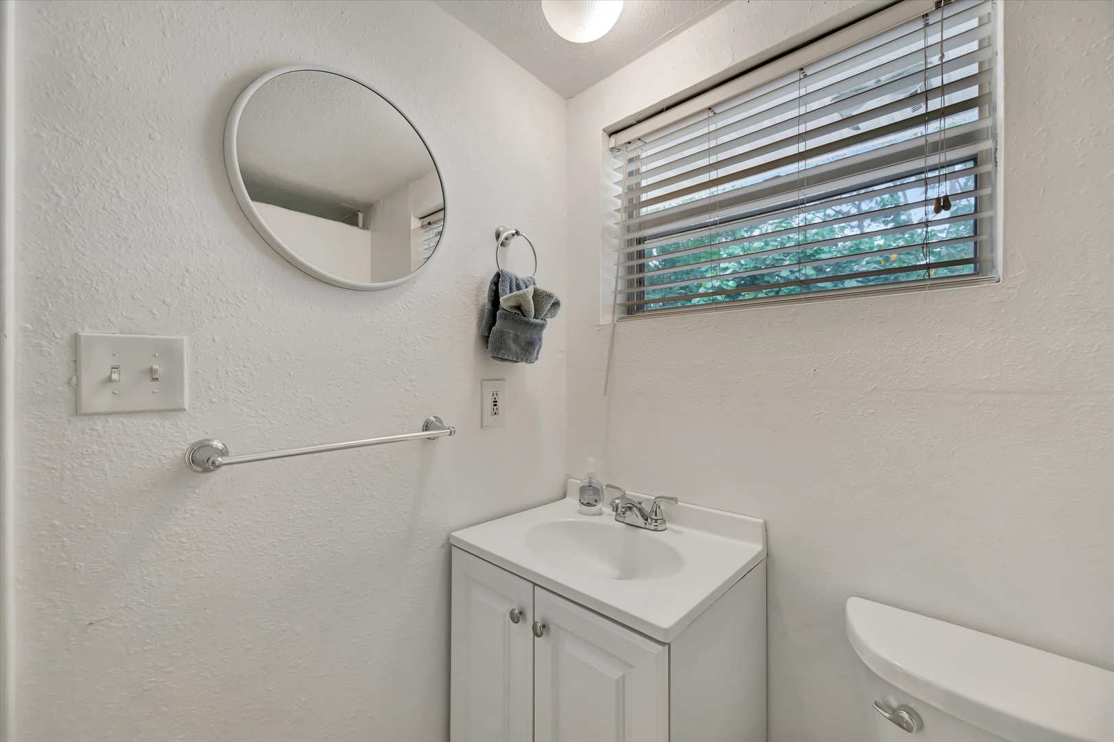 Your private bathroom features fresh white finishes and thoughtful touches, with natural light filtering through the window to create a clean, welcoming space.