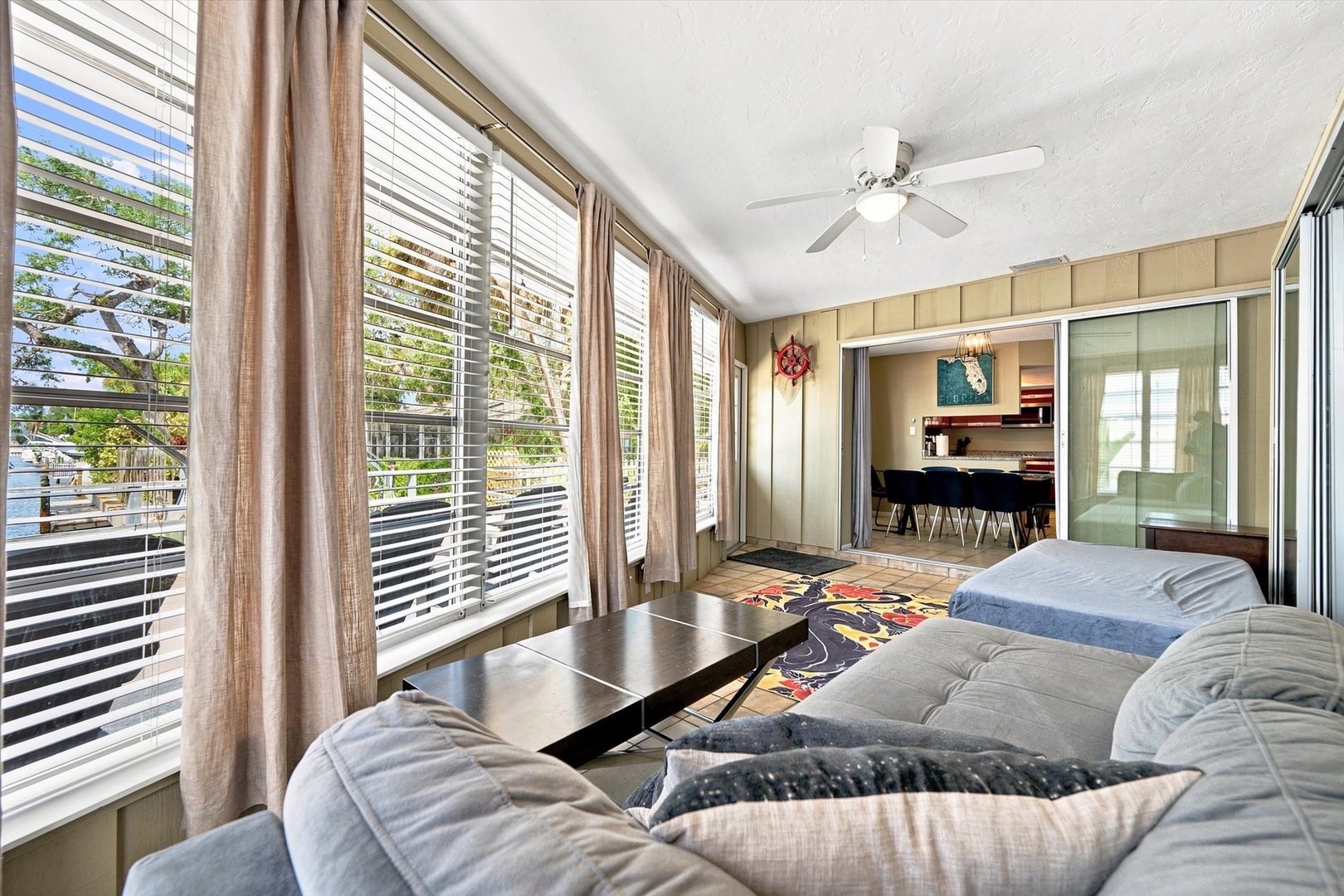 Sink into plush seating in your sunlit lounge, where breezy blinds frame leafy neighborhood views and easy flow into the modern kitchen invites relaxed coastal living.