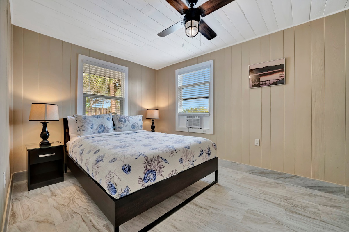 Drift off in this coastal-inspired bedroom where soft nautical linens, warm lamplight, and a gentle ceiling fan set the scene for your most restful nights.