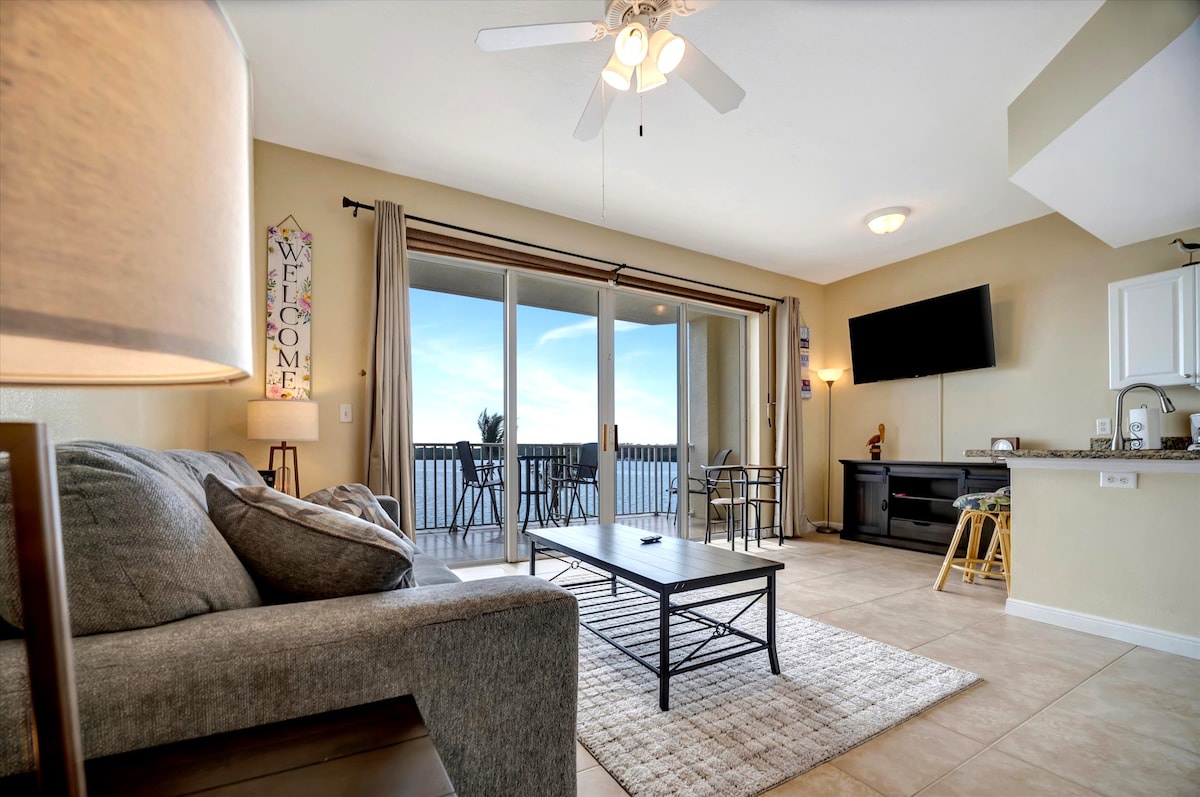 Step into your open-concept retreat where soft coastal light fills the room. Sink into the plush sofa, enjoy meals at the bar, and step through glass doors to your private balcony with water views.