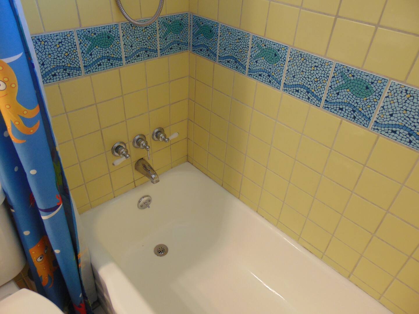 Soak away your cares in this charming tub, featuring cheerful yellow tiles and playful mosaic sea creature accents that bring a smile to bath time.