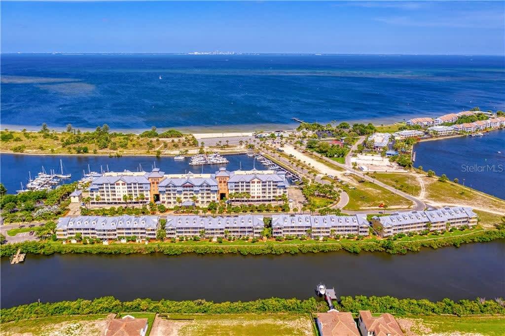 This waterfront property complex sits on a scenic peninsula surrounded by deep blue waters, marina, and protected natural coastline beyond.