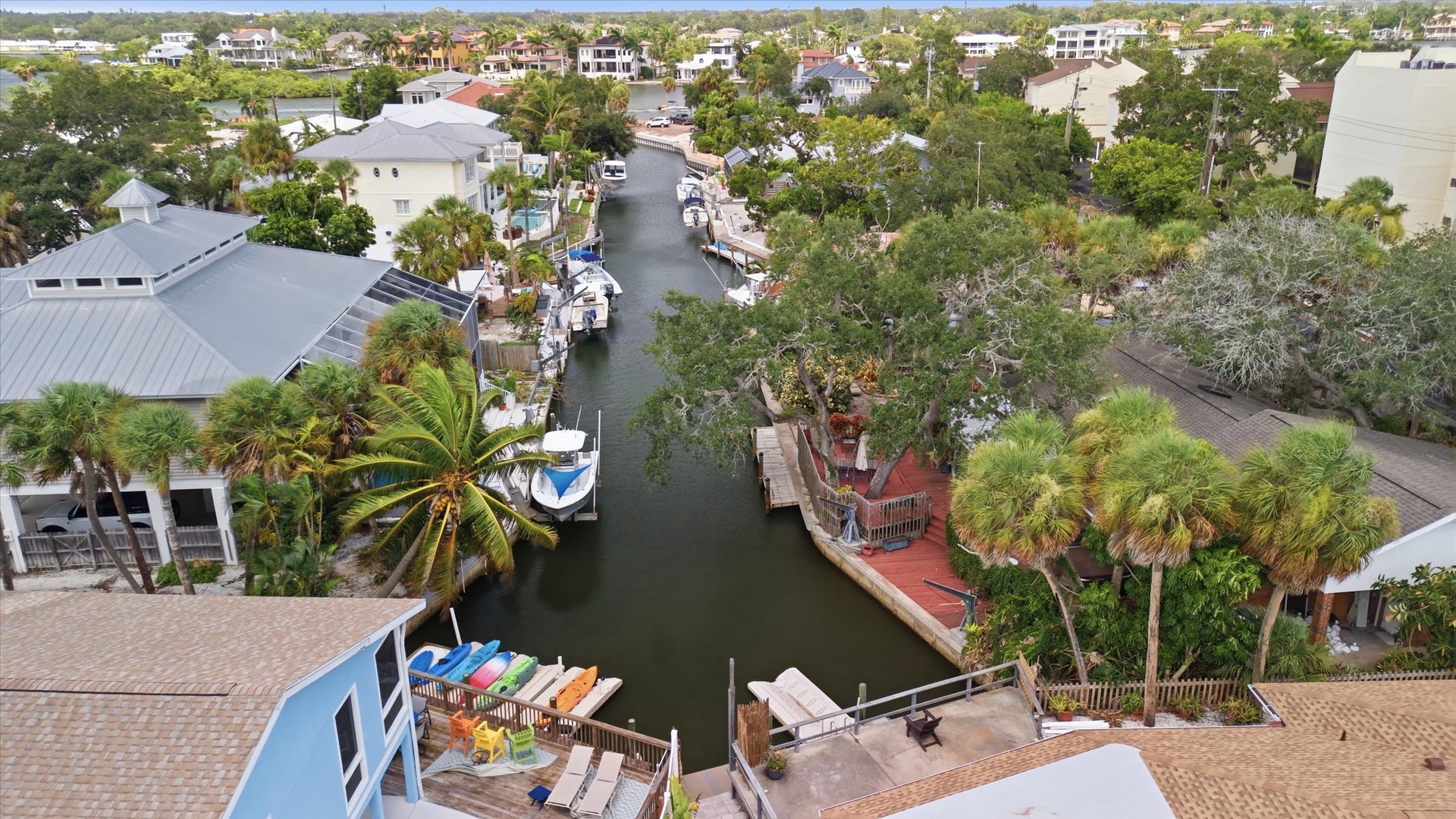 Aerial view of a waterfront neighborhood with canal access, docked boats, and lush tropical greenery surrounding residential properties.