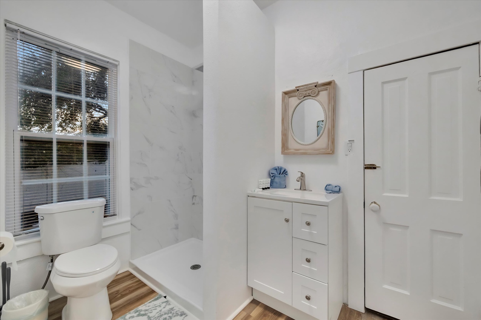 Refresh in your own bright, spotless bathroom—complete with a marble-style shower, warm wood floors, and a vintage-style mirror that adds a personal touch. Serene and ready for your morning routine.