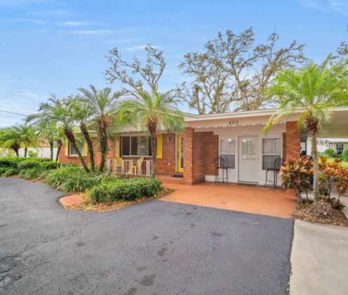 A warm brick property surrounded by lush palms and tropical greenery, welcoming you to your sunny Florida retreat.