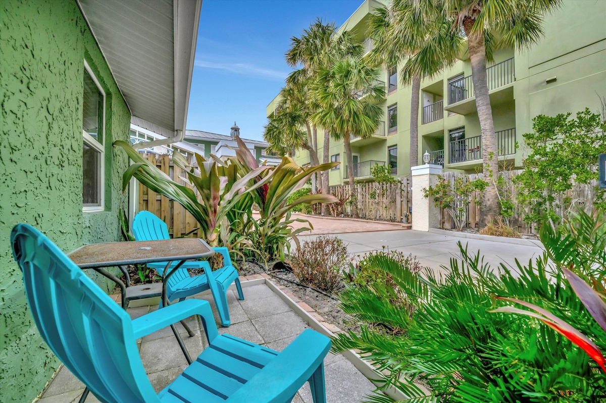 Settle into your private patio with tropical greenery and bright turquoise chairs—a sunny, peaceful spot surrounded by palm trees and coastal charm.