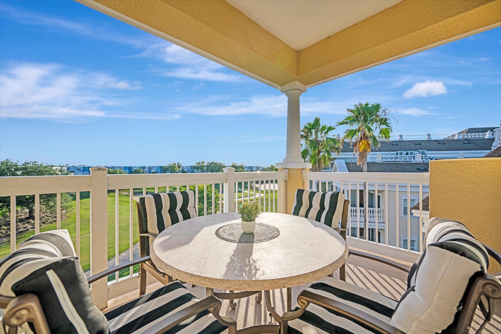 A serene covered balcony framing tropical palm trees and open skies, with outdoor dining ready for your morning coffee or sunset cocktails.