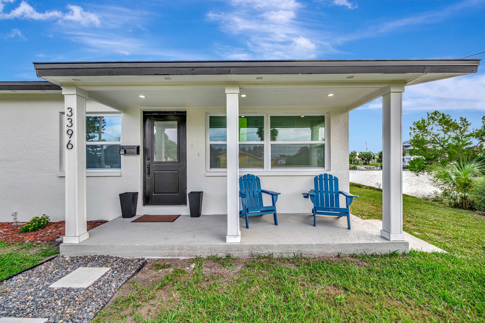 The welcoming covered porch marks the entrance to this coastal retreat, featuring bright blue Adirondack chairs ready for your morning coffee or evening unwind.