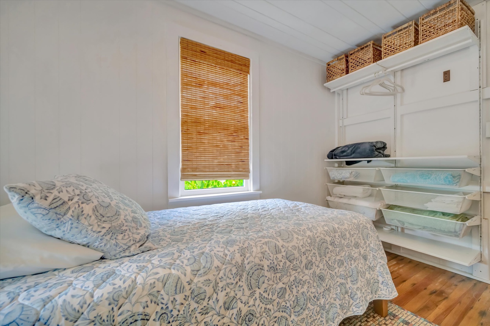 Sink into your cozy bed as gentle light filters through bamboo blinds. Simple, serene, and thoughtfully organized, your personal retreat awaits with open shelving and inviting warmth.