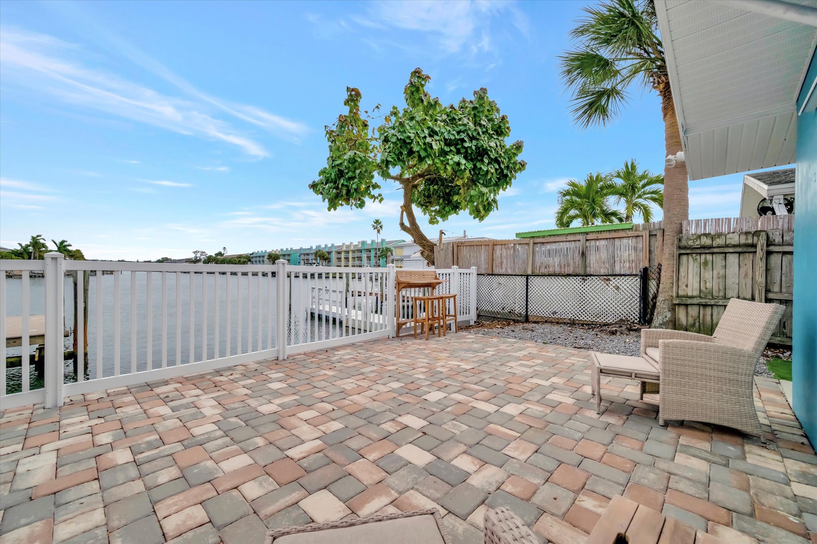 Your private waterfront patio invites you to unwind on spacious pavers, with tropical palms overhead and serene water views stretching beyond the railing—perfect for morning coffee or sunset relaxation.