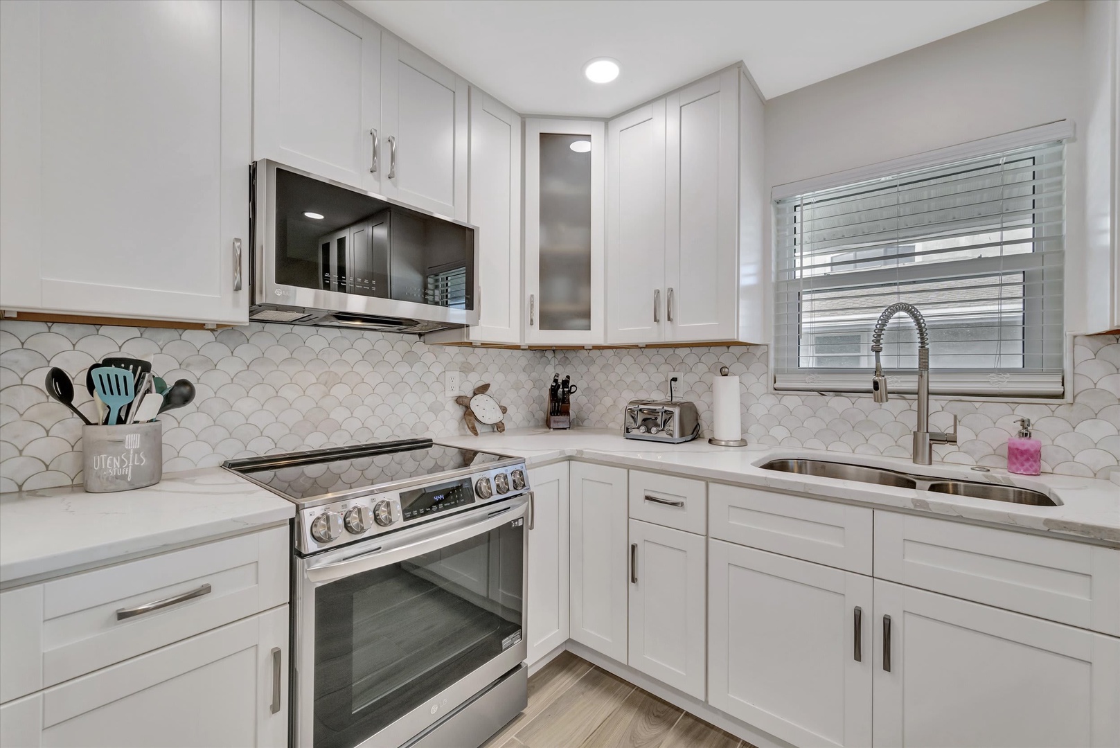 Cook up your favorite meals in this bright, modern kitchen with sleek white cabinetry, stylish scalloped tile backsplash, and gleaming stainless steel appliances ready for your culinary adventures.