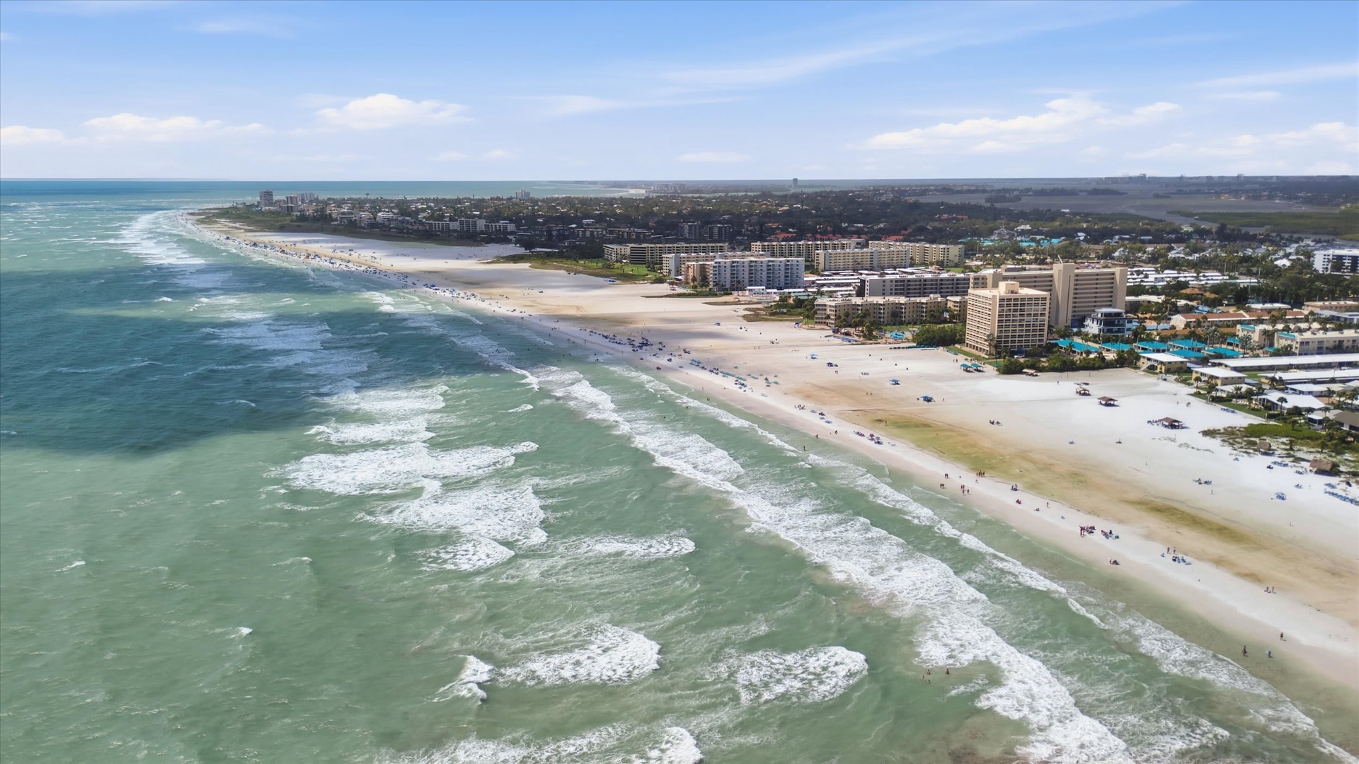 An aerial view showcasing the stunning beachfront location and surrounding coastal community. The property is situated near pristine sandy shores with turquoise waters.