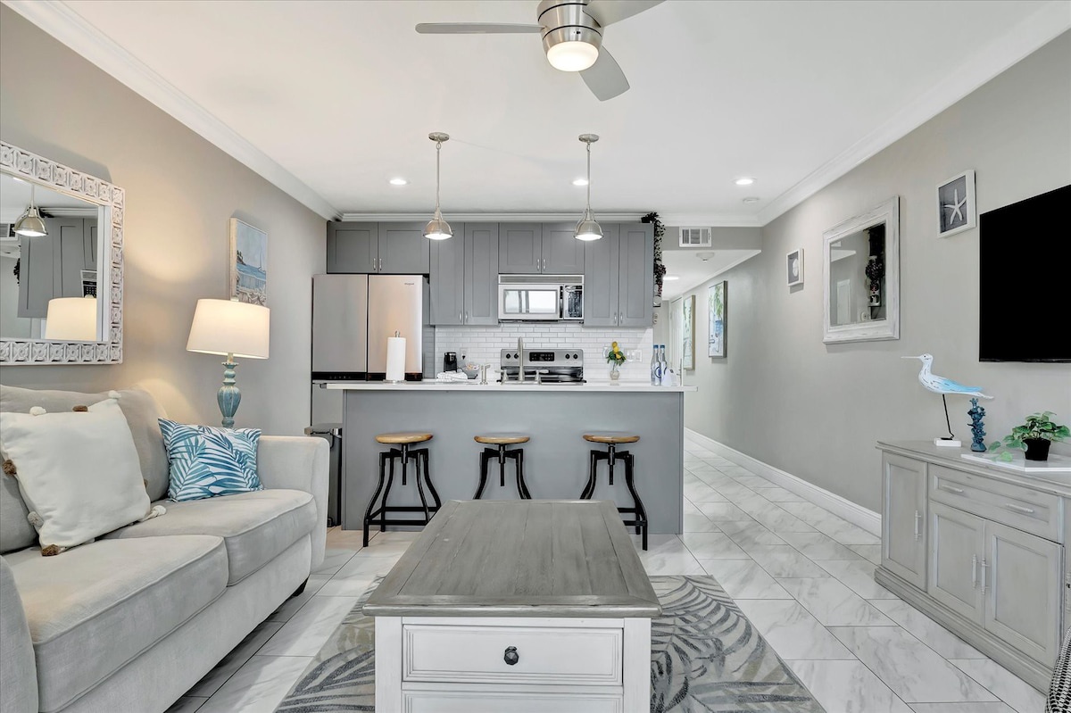 Your open-concept living space blends comfort and style, where soft coastal hues meet modern finishes. Relax on the sofa or gather at the kitchen bar—everything flows effortlessly for your stay.