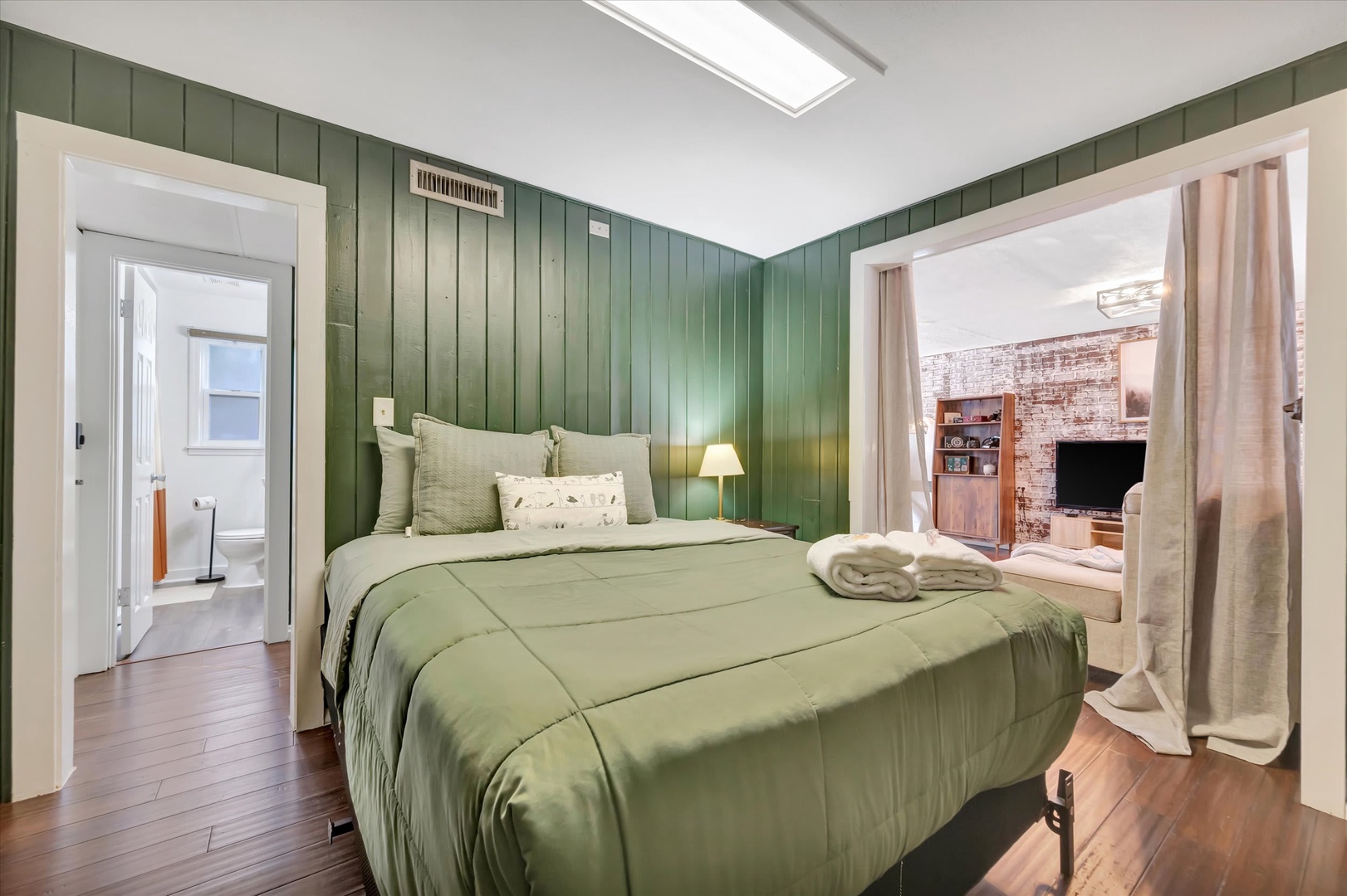 Unwind in your serene bedroom with soothing green tones, plush bedding, and natural light streaming through the skylight. Thoughtful touches like fresh towels and elegant paneling help you feel right at home.