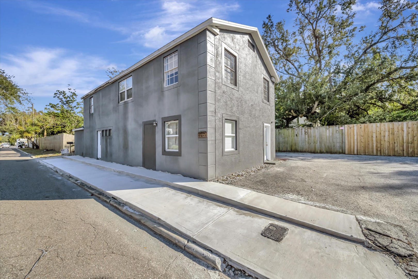 A two-story property with a modern gray facade and white trim, located on a quiet residential street with mature trees providing natural shade and a peaceful ambiance.