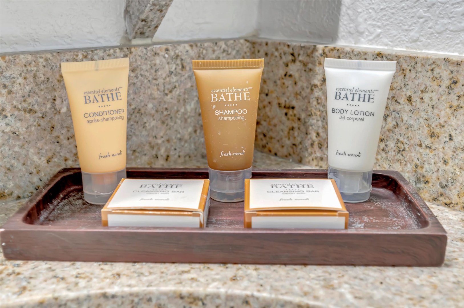Fresh-scented bath amenities await, with quality shampoo, conditioner, body lotion, and soap arranged neatly on a wooden tray for your refreshing stay.