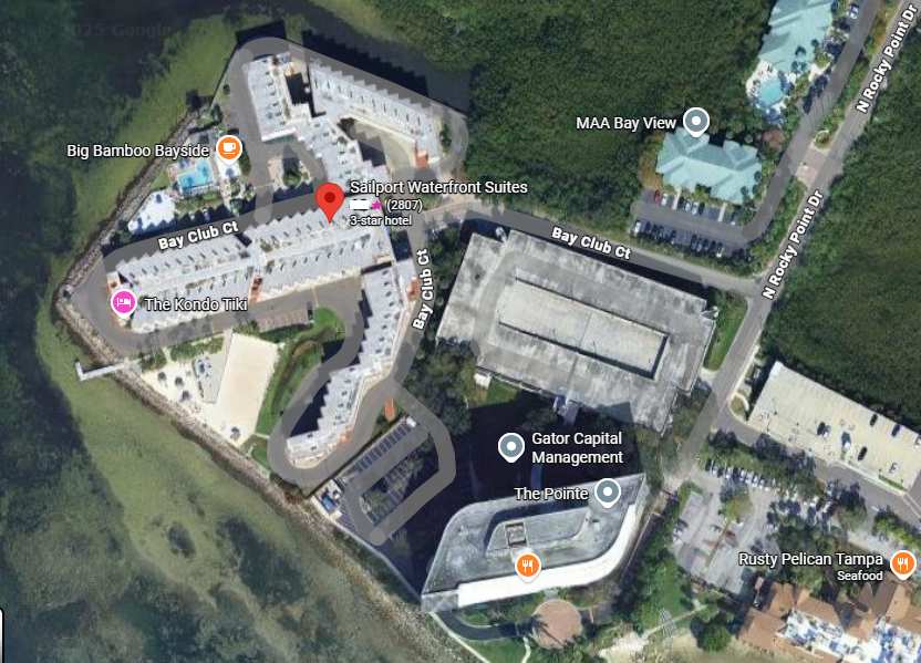 Aerial view of Sailport Waterfront Suites situated within a resort complex near the bay, surrounded by tropical vegetation and neighboring amenities.