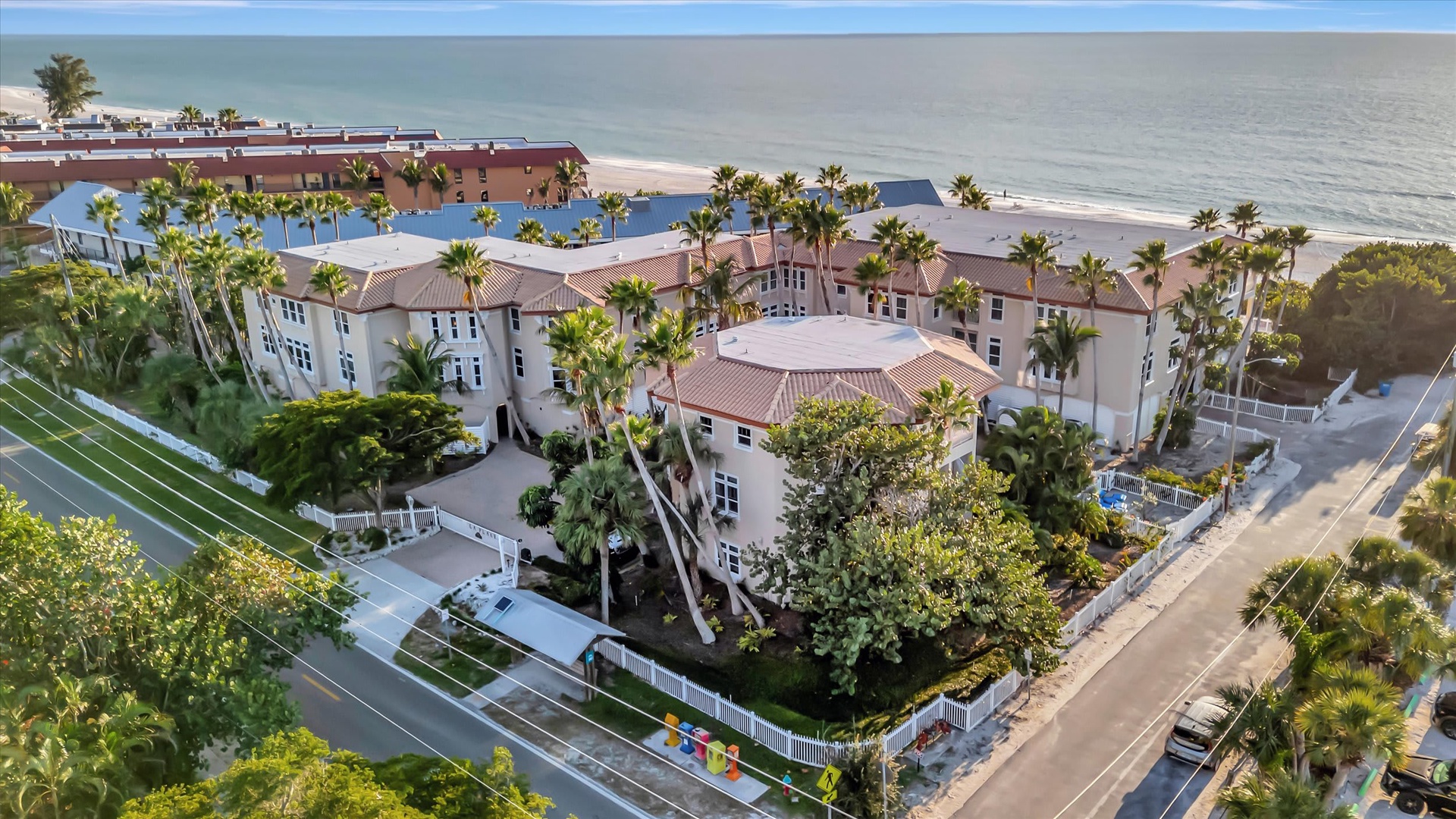 An aerial view captures this beachfront property nestled among swaying palms, just steps from the sandy shore and calm Gulf waters.