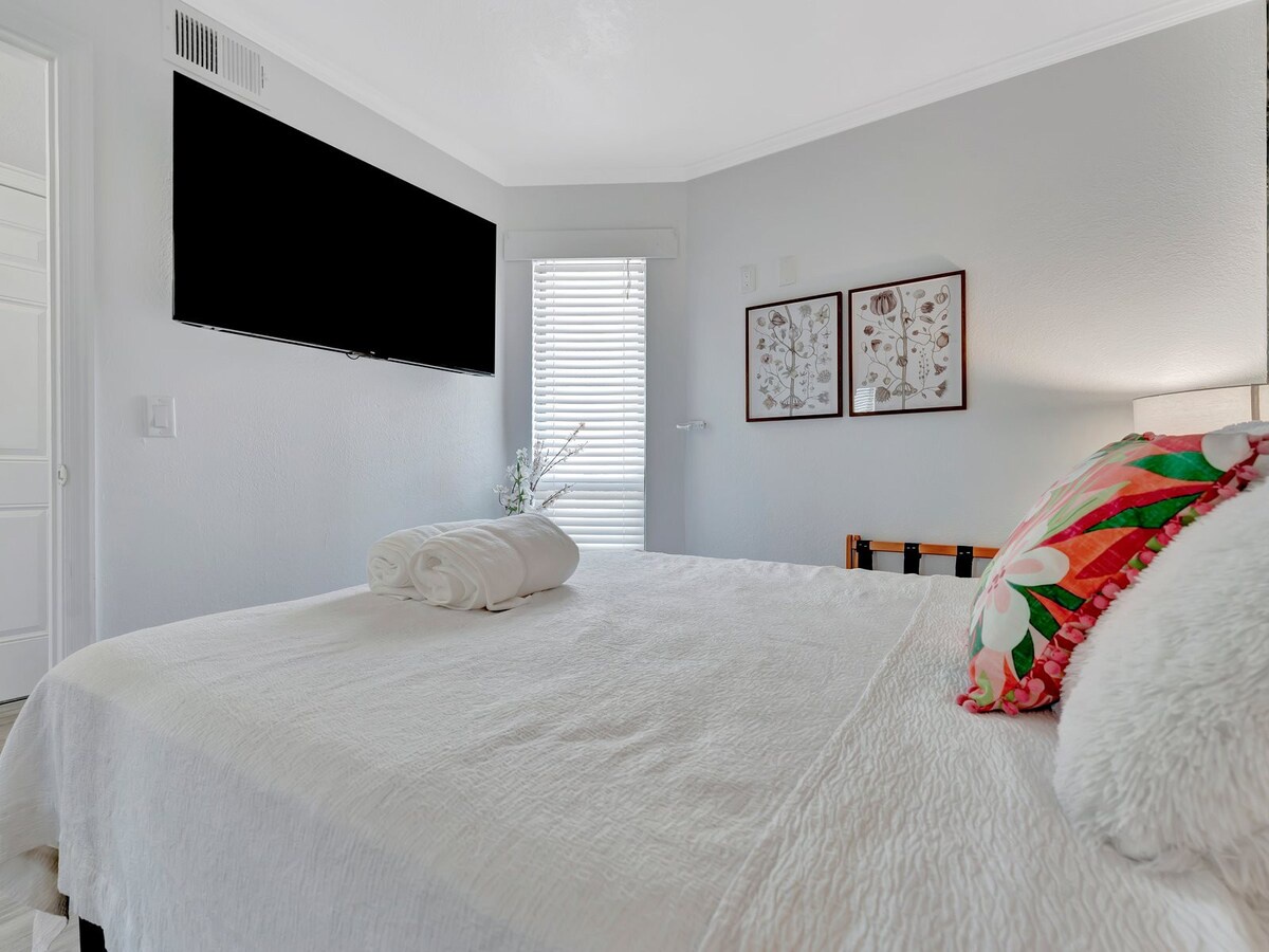 Sink into crisp white linens in your serene bedroom retreat. Soft natural light filters through the blinds, while thoughtful touches like fresh towels and cheerful décor help you settle in and unwind after a day of exploring.