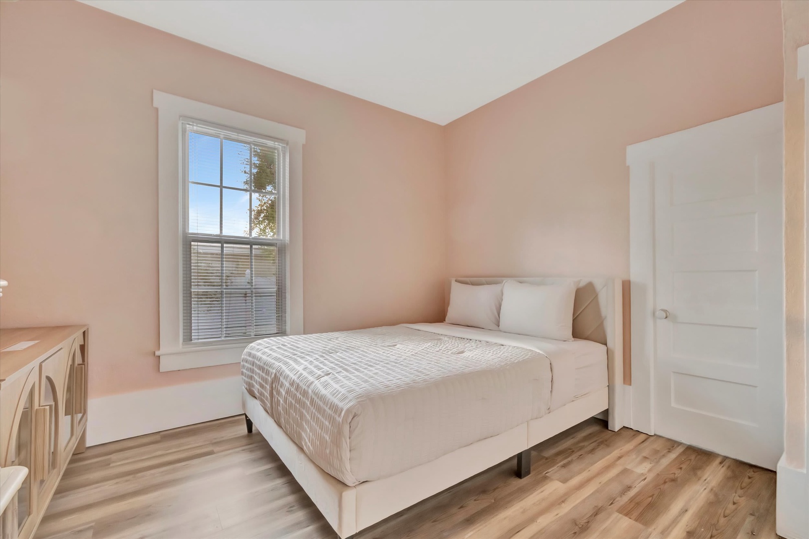 Sink into the plush bedding and let soft peach tones wrap you in warmth. Natural light from the window brightens your mornings, while the peaceful setting invites restful nights.