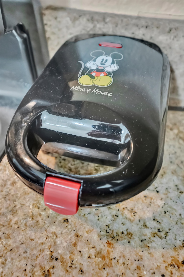 A whimsical Mickey Mouse waffle maker sits ready on the granite counter, perfect for starting your mornings with a little Disney magic and delicious homemade waffles.