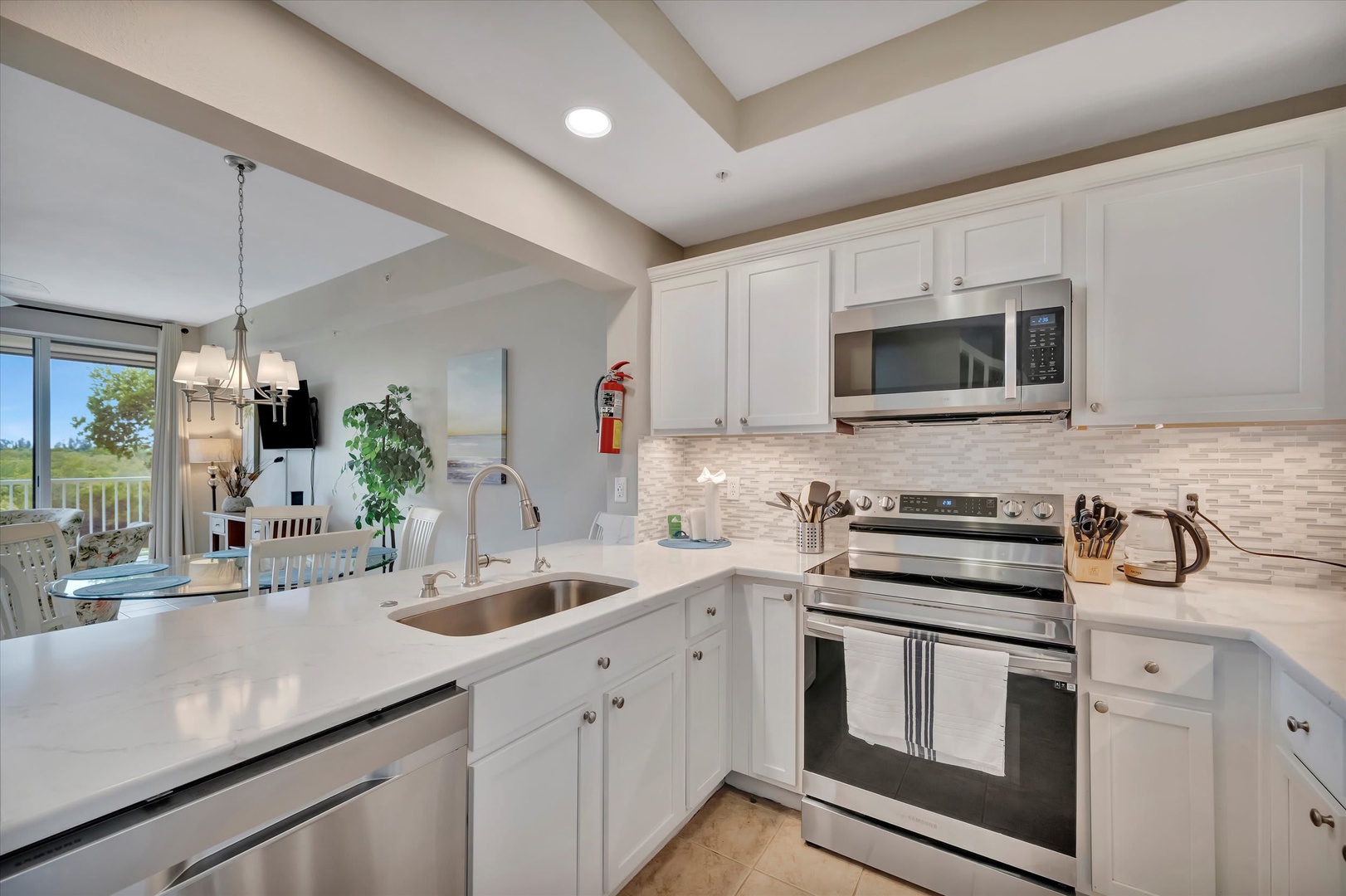 Your fully-equipped kitchen features stainless steel appliances, sleek white cabinetry, and ample counter space for preparing meals together. Sunlight streams through the open layout, creating a bright and welcoming spot to gather.