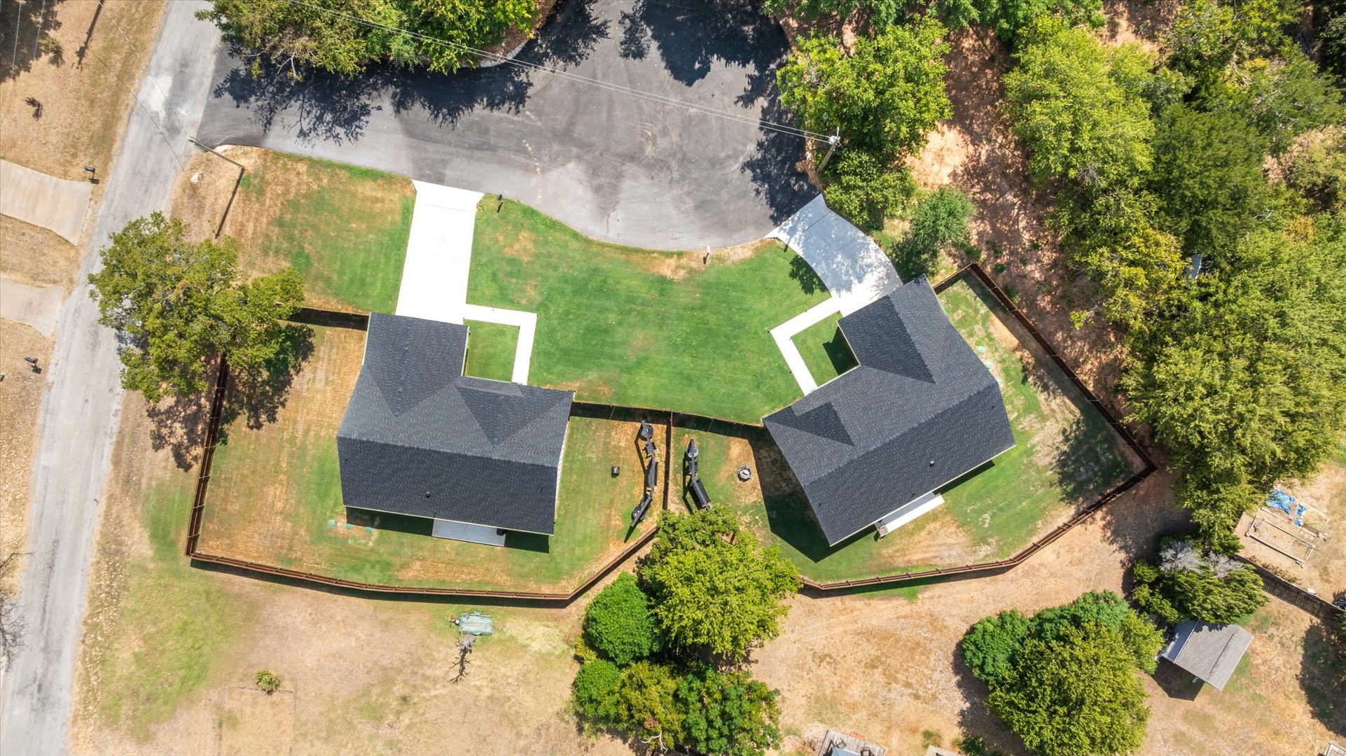 Aerial view showing two separate structures set on a private, tree-lined property with a fenced perimeter and access driveway.