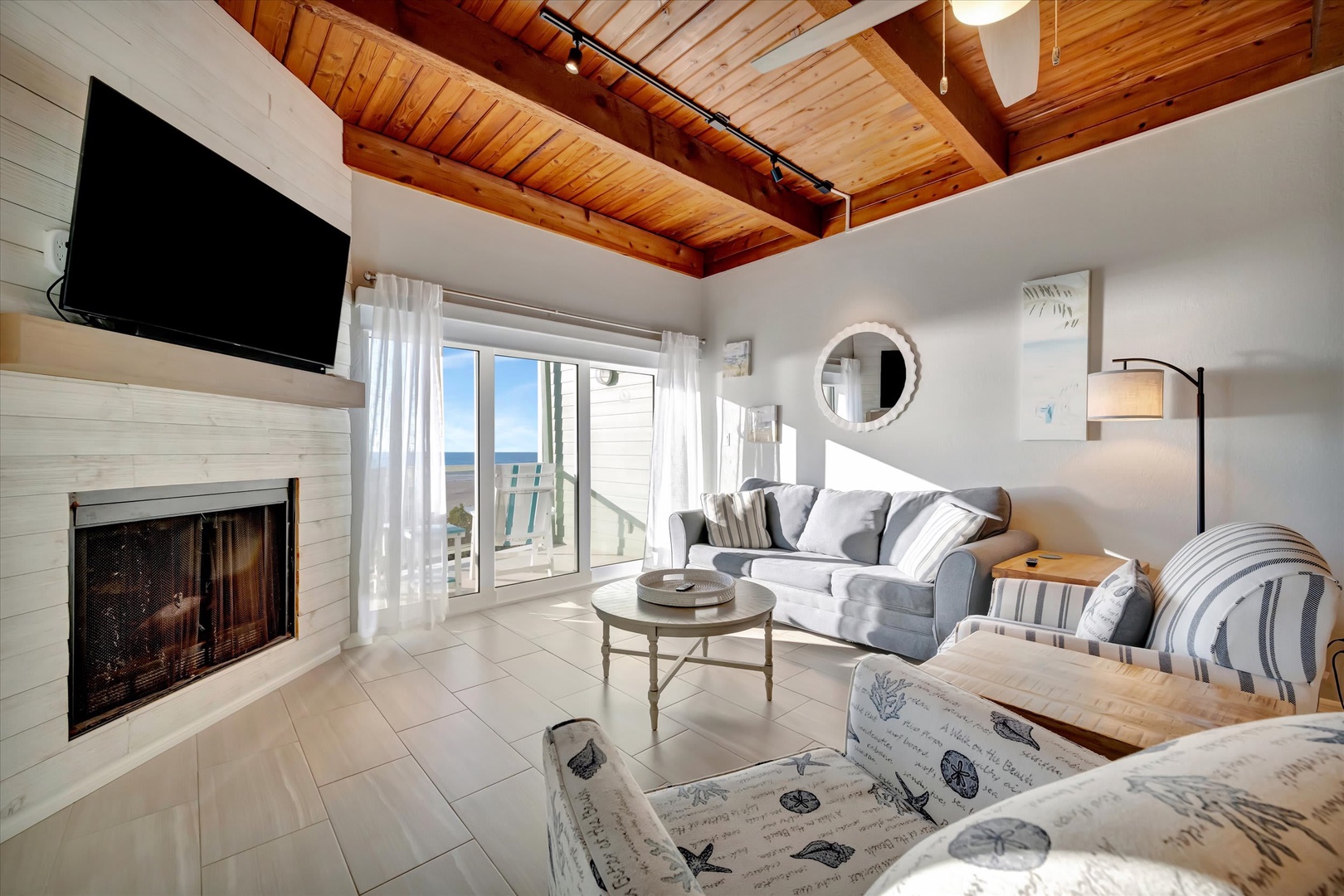 Step into your coastal haven where warm wood beams frame bright ocean views. Curl up by the fireplace or relax on plush seating while natural light fills your airy living space.