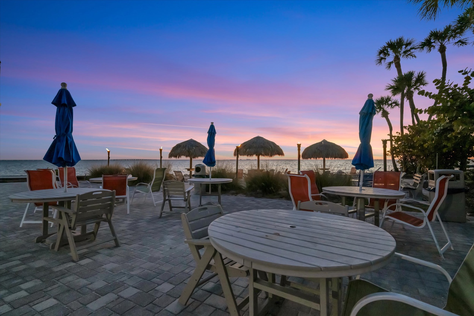 The property's beachfront patio offers a stunning sunset backdrop with palm-shaded seating, tropical tiki huts, and calming waterfront views—perfect for unwinding after a day of exploration.