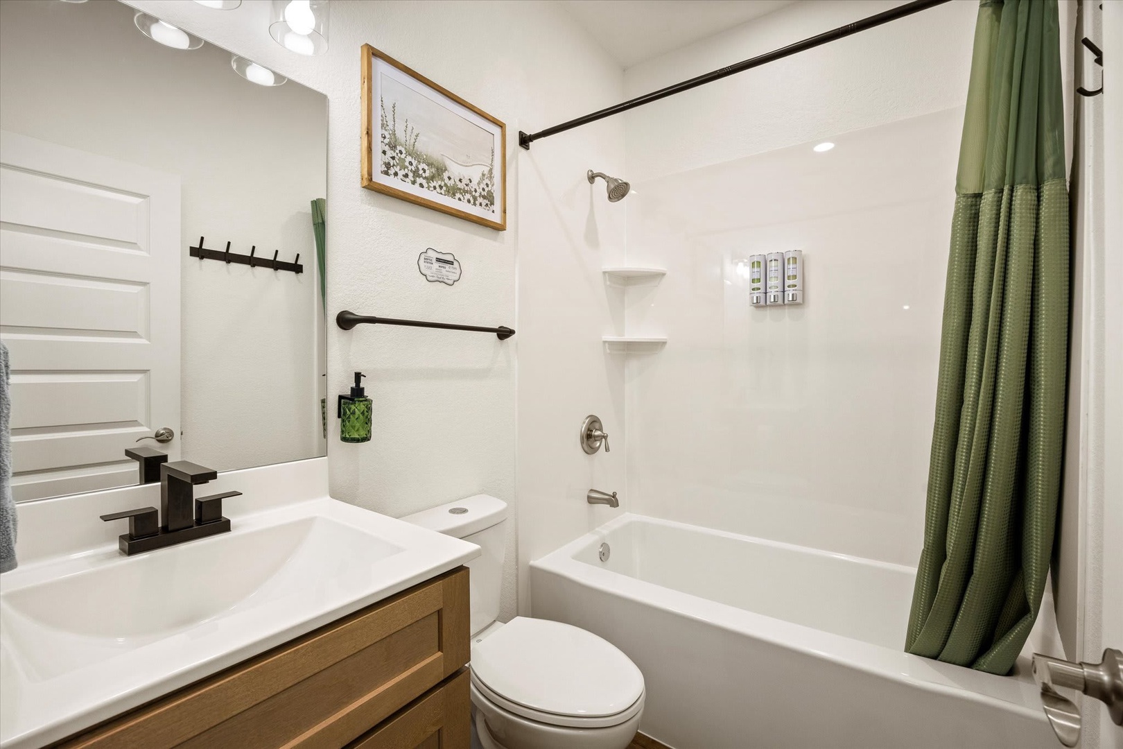 Step into your freshly updated bathroom with crisp white tile, a sleek tub-shower combo, and thoughtful touches like botanical artwork and modern fixtures that make every refresh feel special.